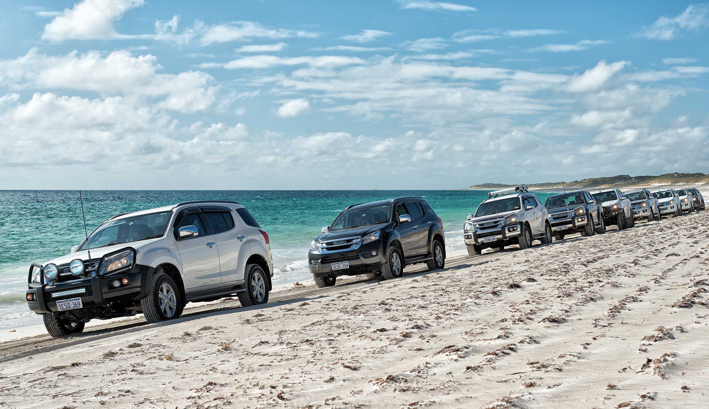 Convoy of Isuzu vehicles drive along beach