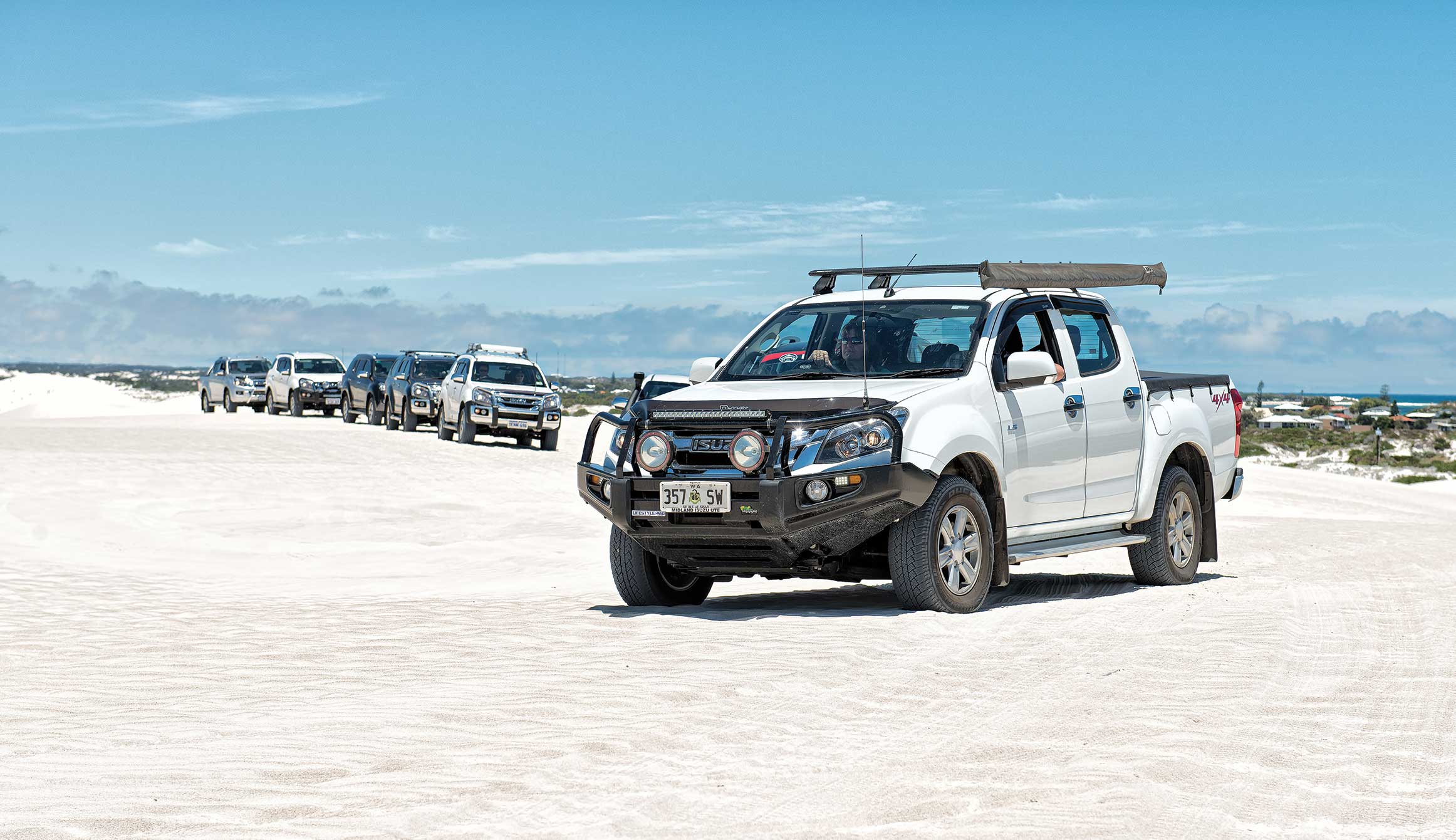 Convoy of Isuzu vehicles drive along sand 