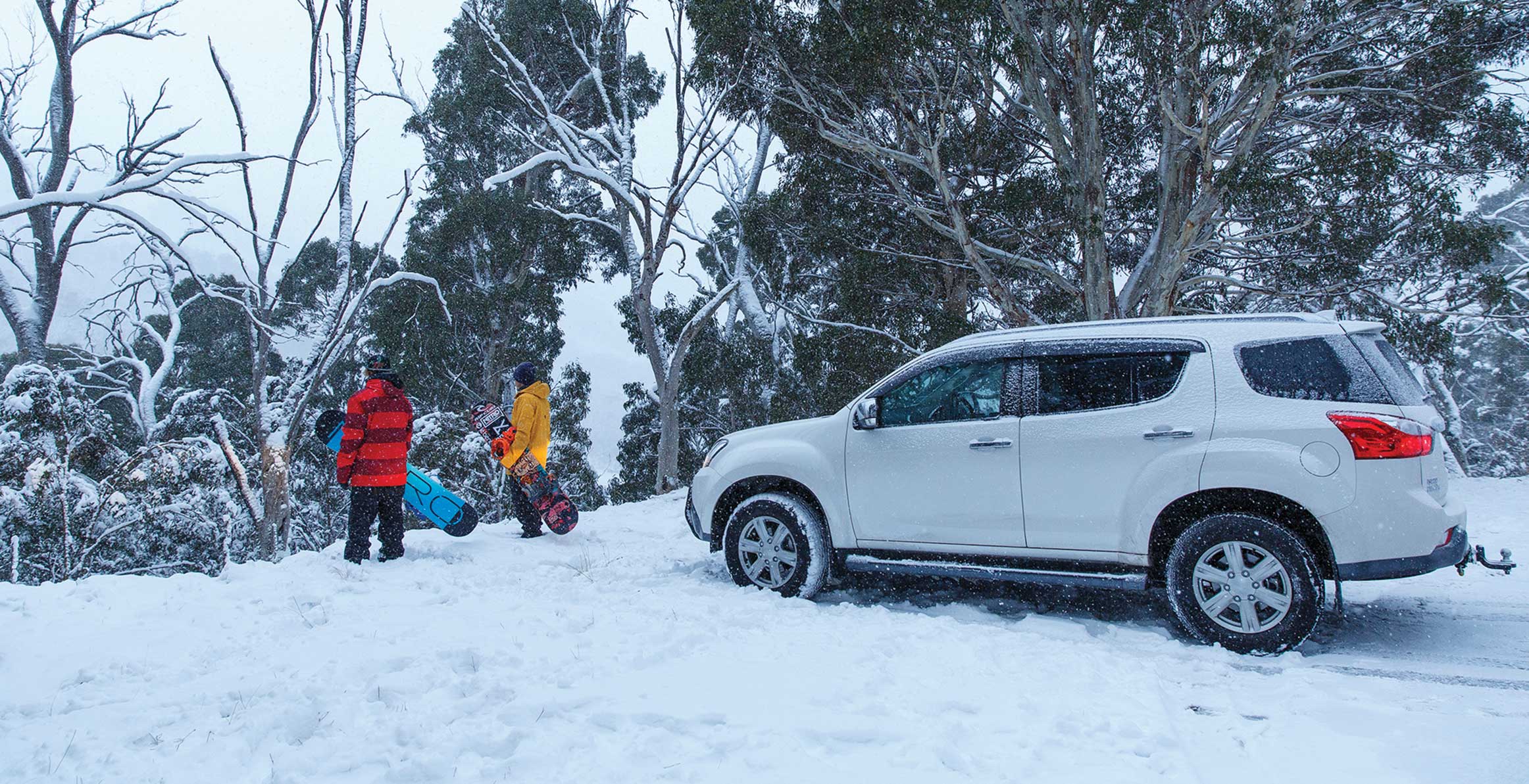 Two snowboarders stand in front of the MU-X in the snow