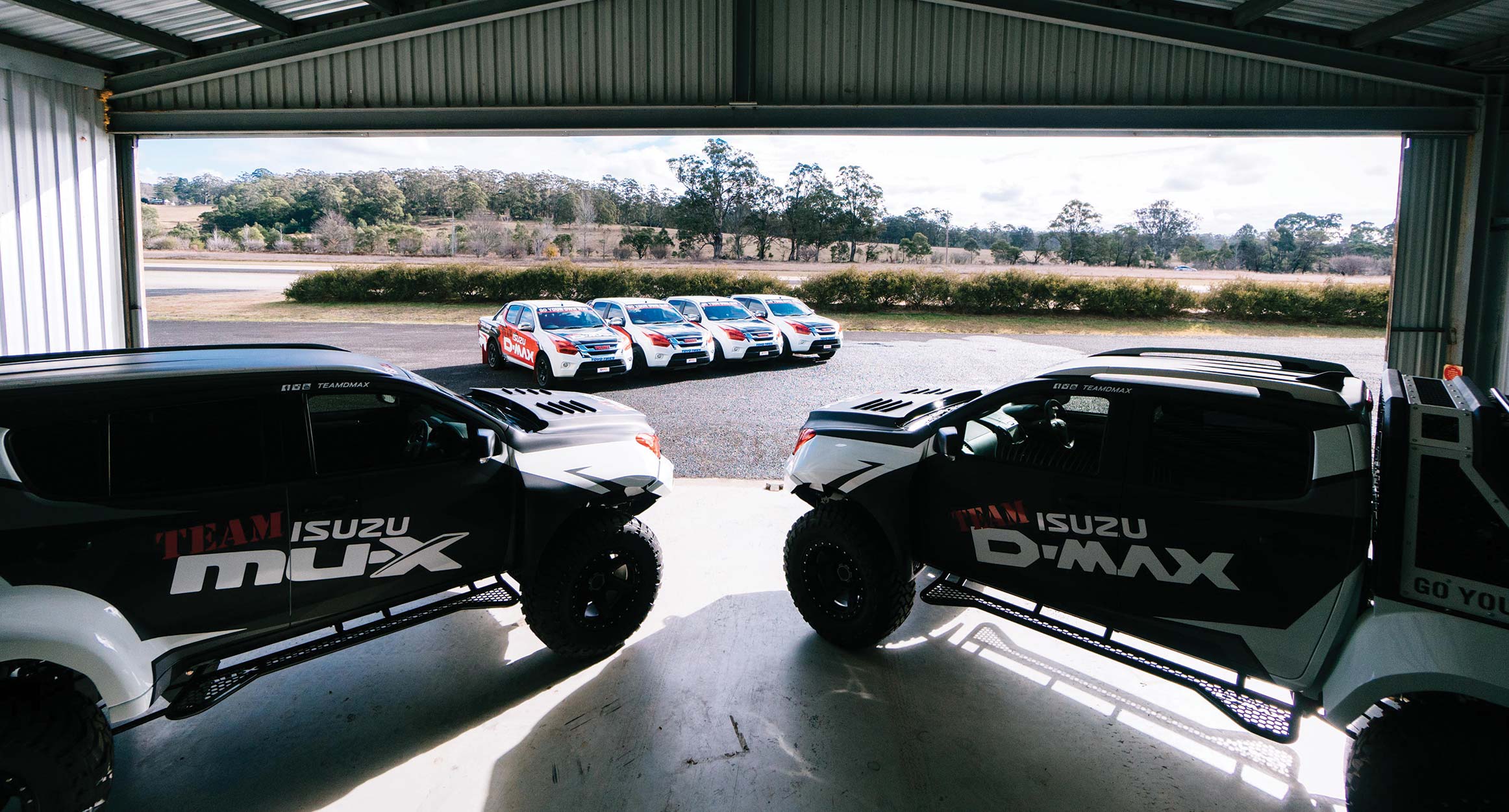 Concept-X Team Isuzu vehicles parked in large shed 