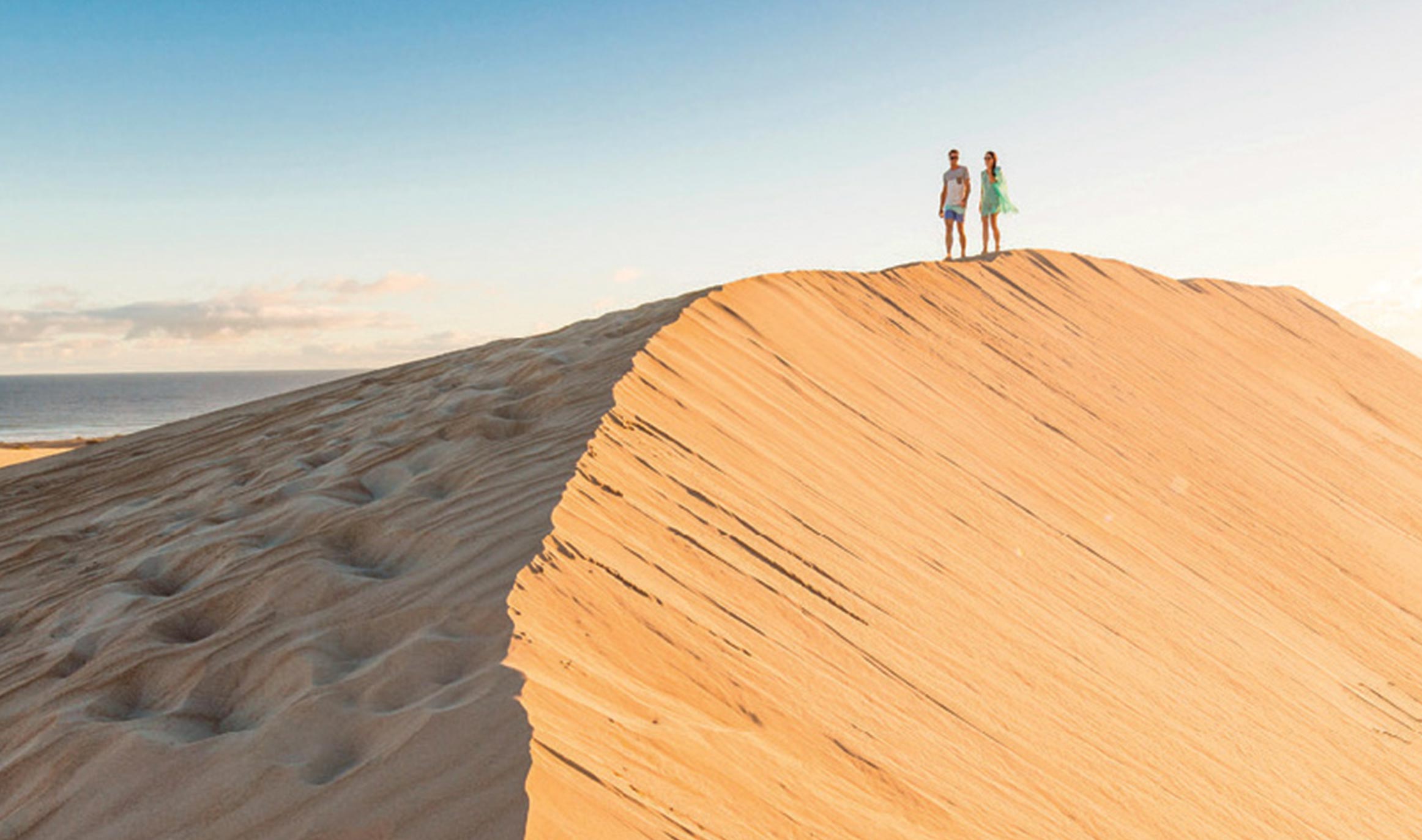 Two people walk along the ridge of a lone sand dune 
