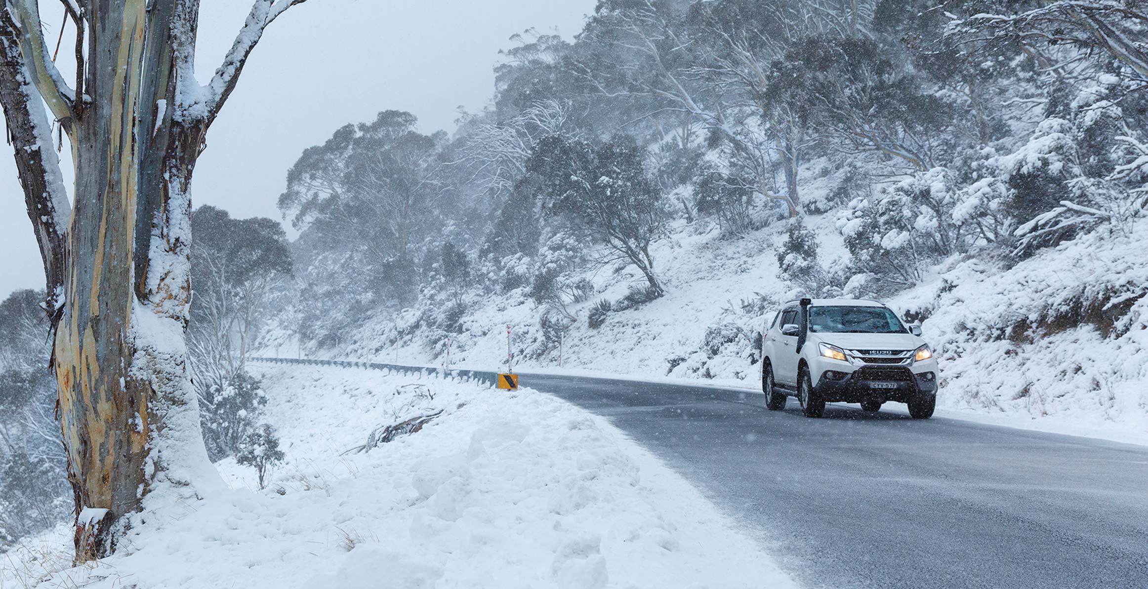 Wide shot of MU-X driving on snowy cliff road 