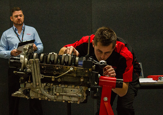 Contestant bends down to work on Isuzu Ute engine in competition
