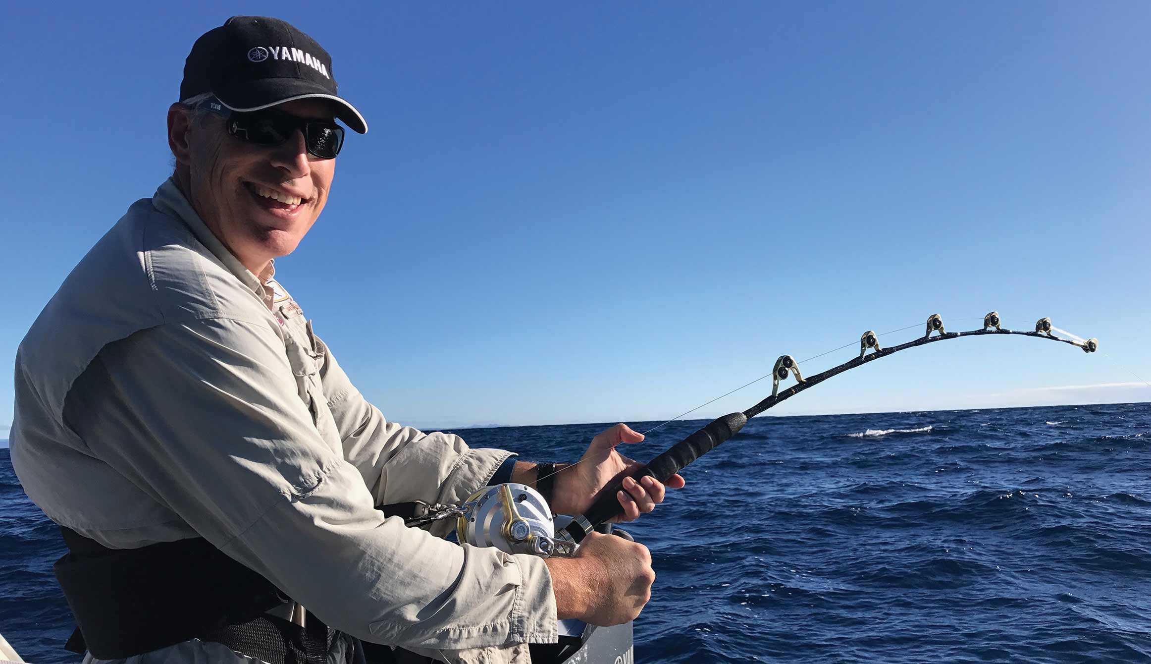 Nick smiles on the boat whilst his rod bends in the water