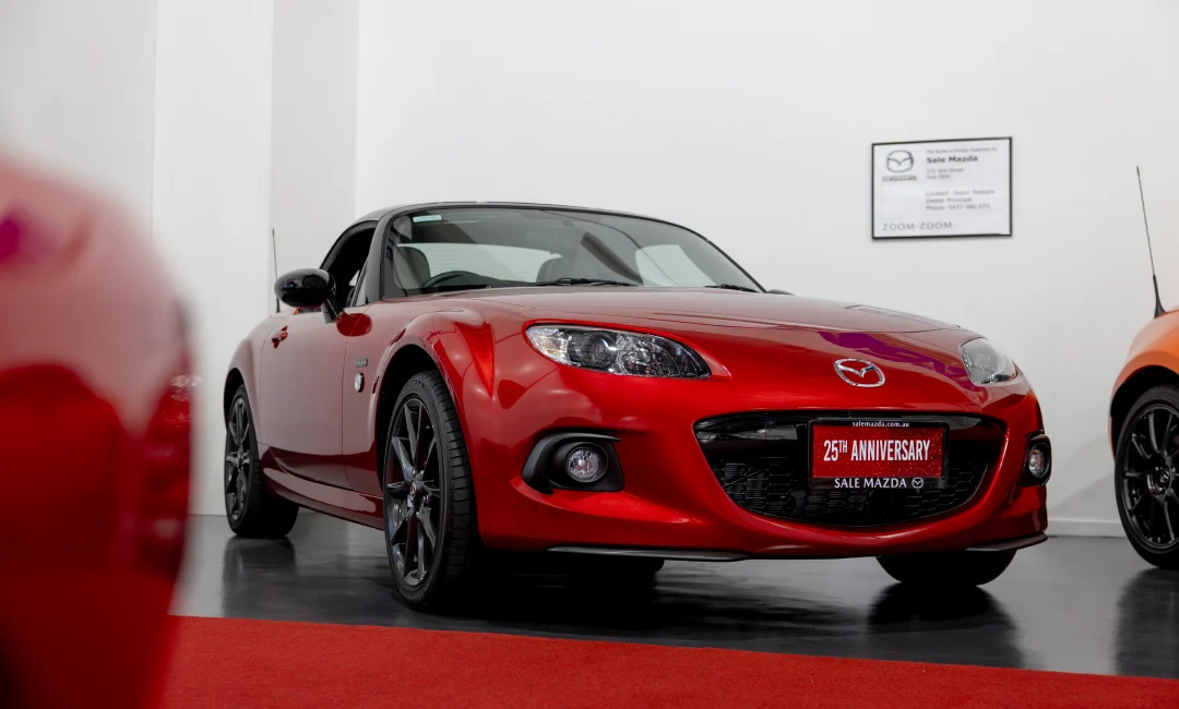 Mazda MX-5 25th Anniversary Edition in vibrant red displayed indoors on a red carpet, featuring sleek black alloy wheels and commemorative badging, part of Australia’s greatest MX-5 collection.