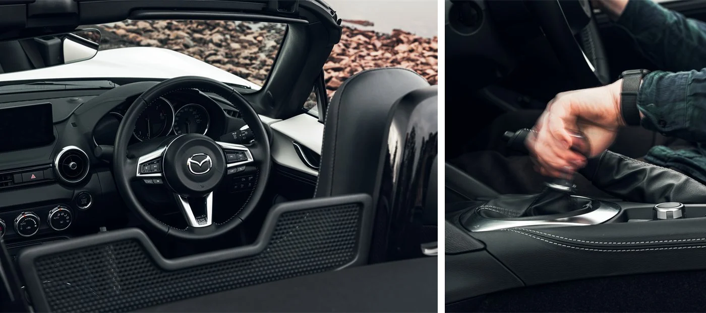 Mazda MX-5 cabin — the leather steering wheel with Mazda badge, beside the six-speed manual gearshift.