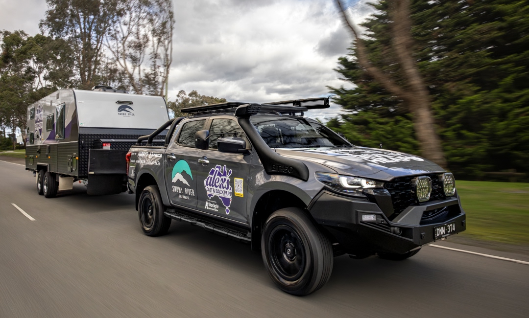 Mazda BT-50 towing a caravan along a lush, tree-lined scenic route, showcasing Snowy River Caravans and Alex's Outback Run branding — ideal for outdoor adventure and caravan lifestyle promotions.