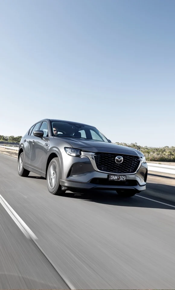 Mazda CX‑60 PHEV driving along a scenic road, highlighting its dynamic performance and elegant design in motion