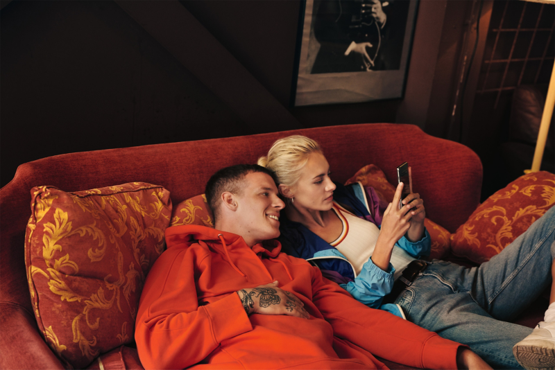 A couple sat on a couch looking at a phone